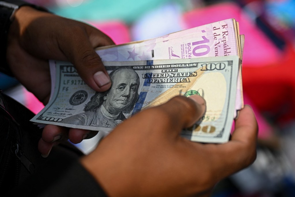 (FILES) A vendor counts Venezuelan bolivar and US dollar banknotes at La Hoyada market in Caracas on December 23, 2025.