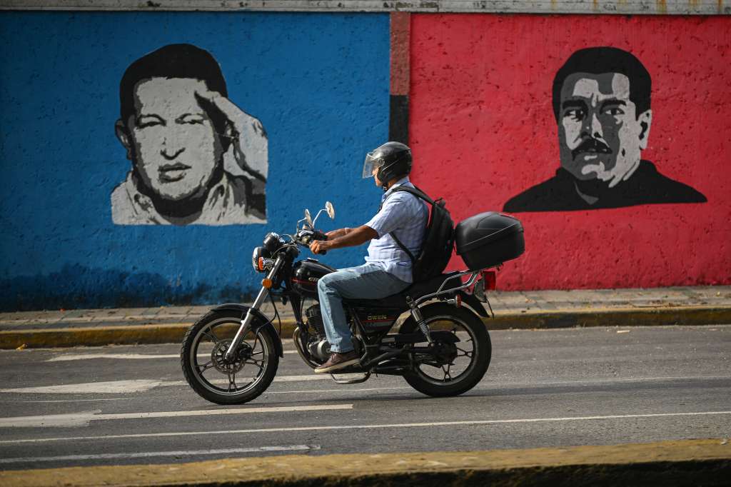 A motorcyclist rides past a mural depicting late Venezuelan President Hugo Chavez (1954-2013) and Venezuelan President Nicolas Maduro (R) in Caracas on September 26, 2024.