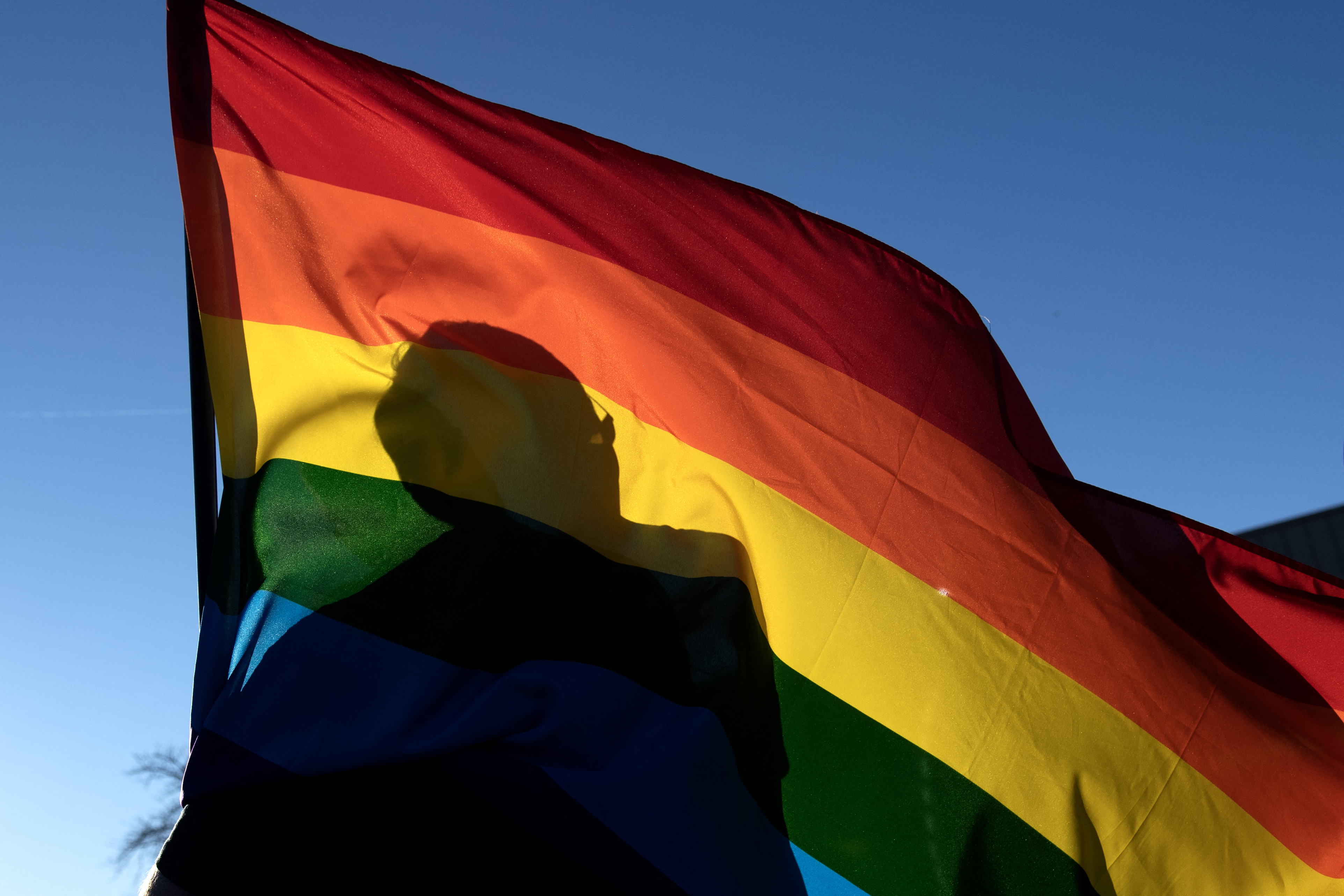 La silueta de un miembro de la comunidad se ve a través de una bandera del Orgullo mientras presenta sus respetos a las víctimas del tiroteo masivo en el Club Q, un club nocturno LGBTQ, en Colorado Springs, Colorado, el 20 de noviembre de 2022.