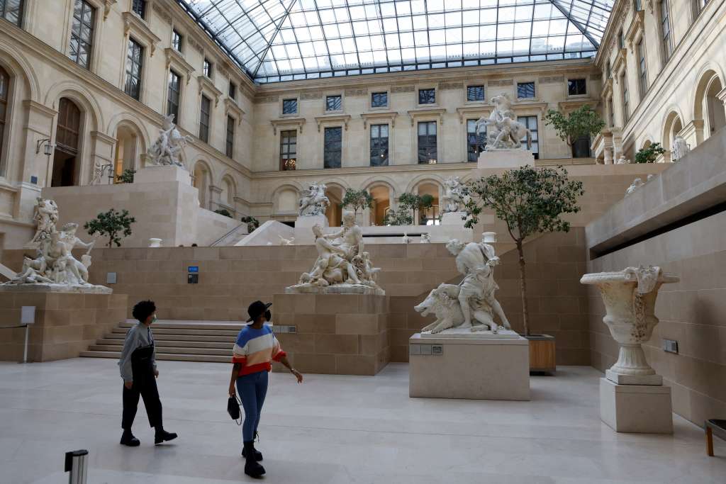 (FILES) Visitors wearing protective face masks look at statues inside the deserted Louvre Museum as the novel coronavirus Covid-19 pandemic keeps the tourists away, in Paris on October 14, 2020.