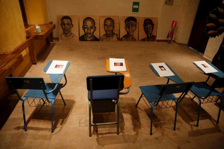 Vista hoy de unos pupitres vacíos con cuadernos y la imagen de cada uno de los cinco jóvenes masacrados en Llano Verde, durante un acto de homenaje a las víctimas de la masacre, en Cali.