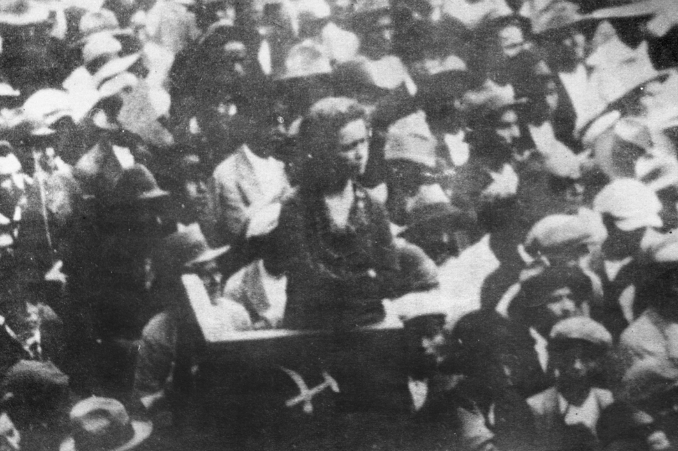 María Cano sobre una tarima rodeada de seguidores en un acto público. Fotografía publicada en “María Cano. El amanecer de la clase obrera” (Bogotá: Librería Sindical Colombiana, 1985).