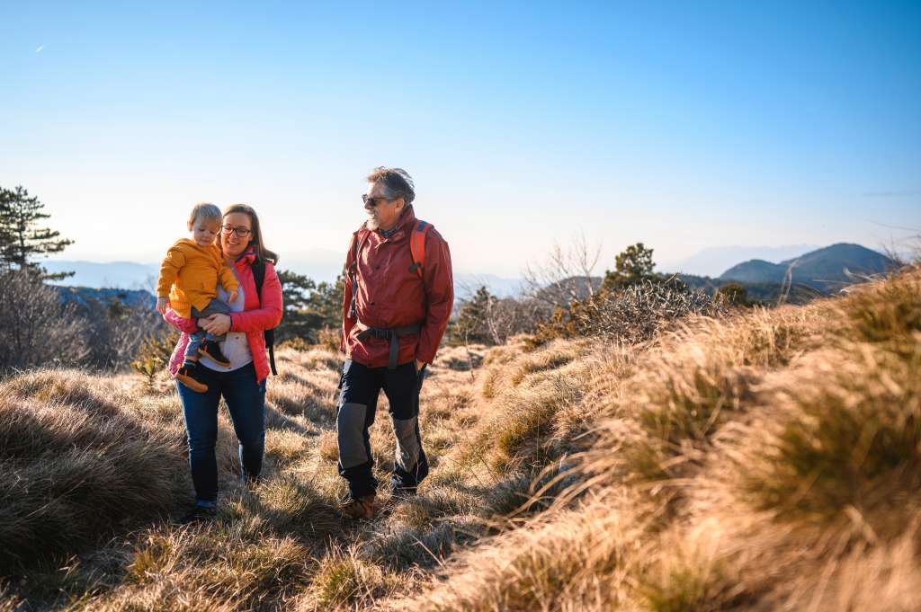 Caucasian multi-generation family walking on a meadow and enjoying time together in nature. They are smiling, happy and holding hands.