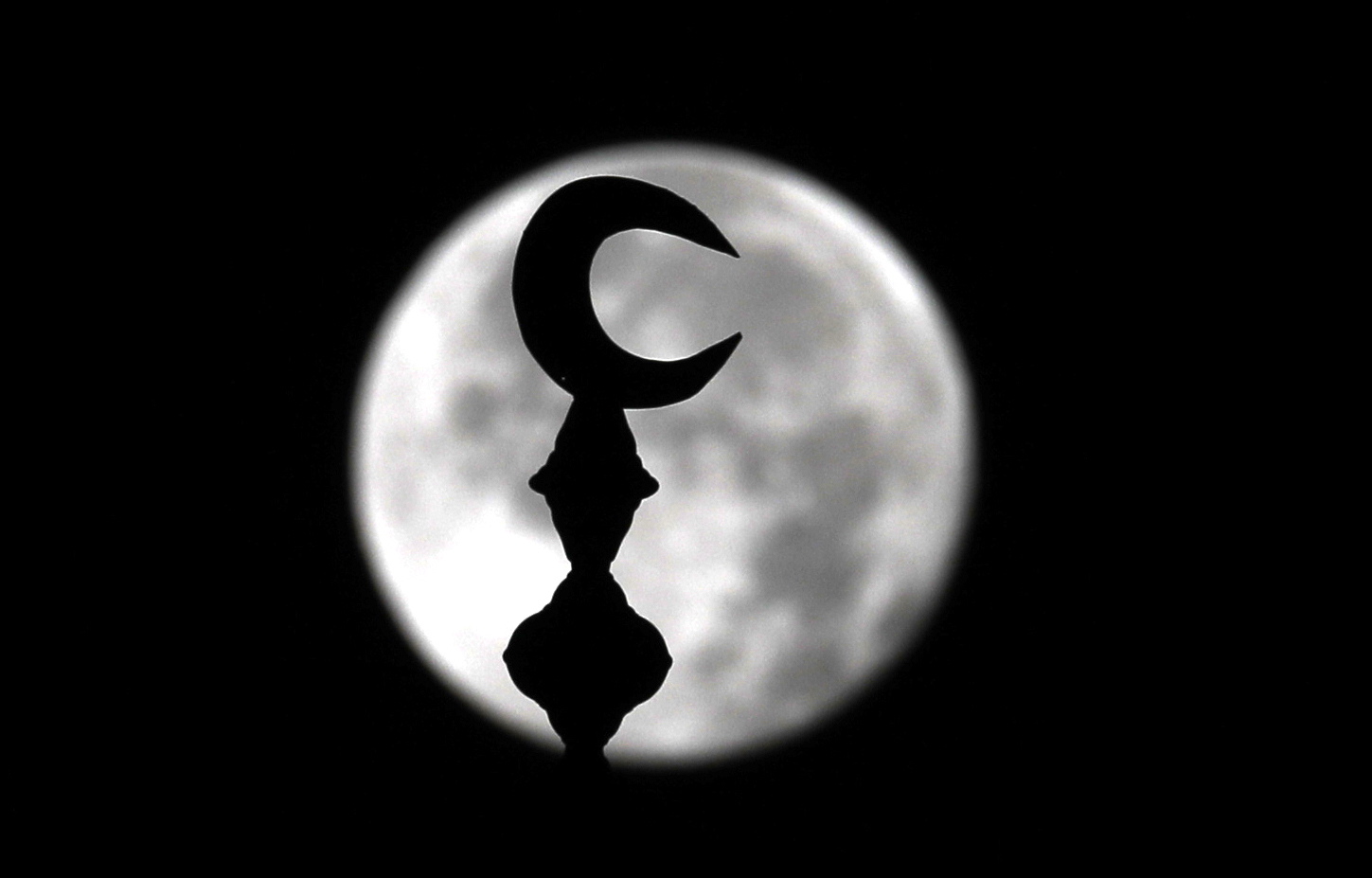 Sana'a (Yemen), 04/07/2023.- La luna llena se oculta tras la media luna en lo alto de una mezquita, en Sana'a, Yemen,este viernes. EFE/YAHYA ARHAB