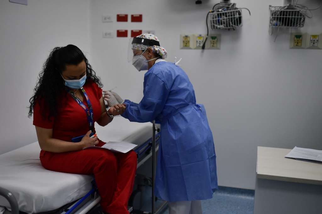 una mujer aplica la vacuna a otra vestida de rojo.