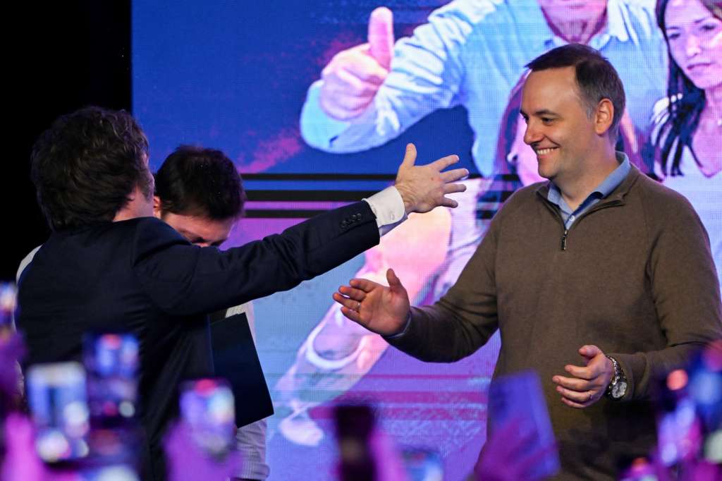 Argentina's President Javier Milei (L) greets Spokesperson for the Presidency Manuel Adorni at the ruling party's La Libertad Avanza headquarters following the results of the national midterm legislative election in Buenos Aires on October 26, 2025.