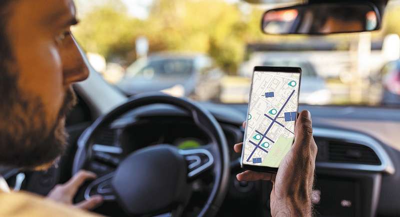 Rear view of unrecognizable Businessman ignoring safety and texting on mobile phone while driving his car, looking at the map.