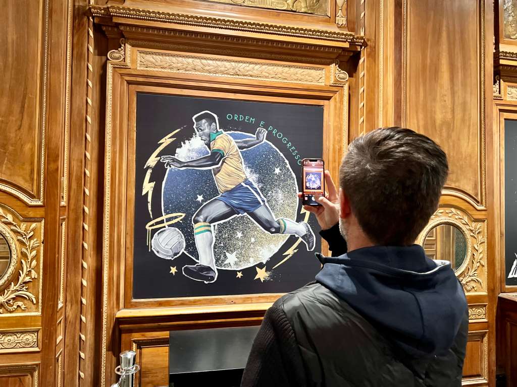 USA2932. NUEVA YORK (NY, EEUU), 30/12/2022.- Un hombre toma una foto con su teléfono móvil a una pintura donde aparece la imagen del jugador brasileño de fútbol Pelé hoy, en el interior de la tienda Pelé Soccer situada en la icónica plaza de Times Square, en Nueva York (EEUU). Flores amarillas y verdes colgaban de la fachada de la tienda Pelé Soccer de Nueva York, situada en la icónica plaza de Times Square, este viernes en honor al futbolista brasileño Edson Arantes do Nascimento, 'Pelé', que murió el jueves a los 82 años. EFE/ Sarah Yáñez-Richards