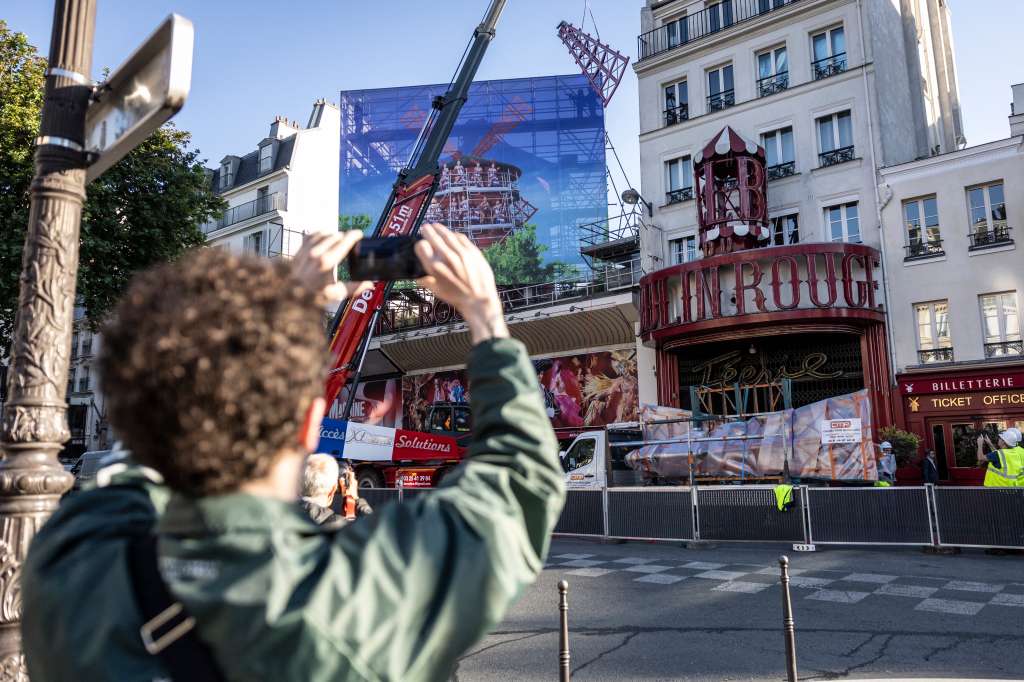 A pedestrian takes a picture of a crane lifting one of the four new windmill sails to install it on the top of the Moulin Rouge cabaret following the collapse of the former ones, in Paris on June 24, 2024.