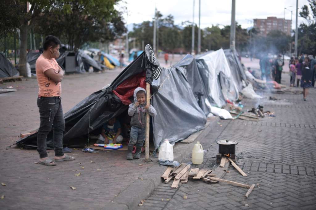 Un indígena mira a un niño que se sostiene de uno de los palos que sostiene un cambuche