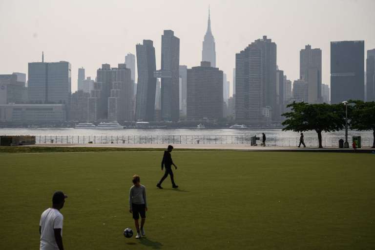 Un grupo de personas juega al fútbol ante el horizonte de la ciudad de Nueva York y el East River envueltos en humo, en Brooklyn, el 5 de junio de 2023.